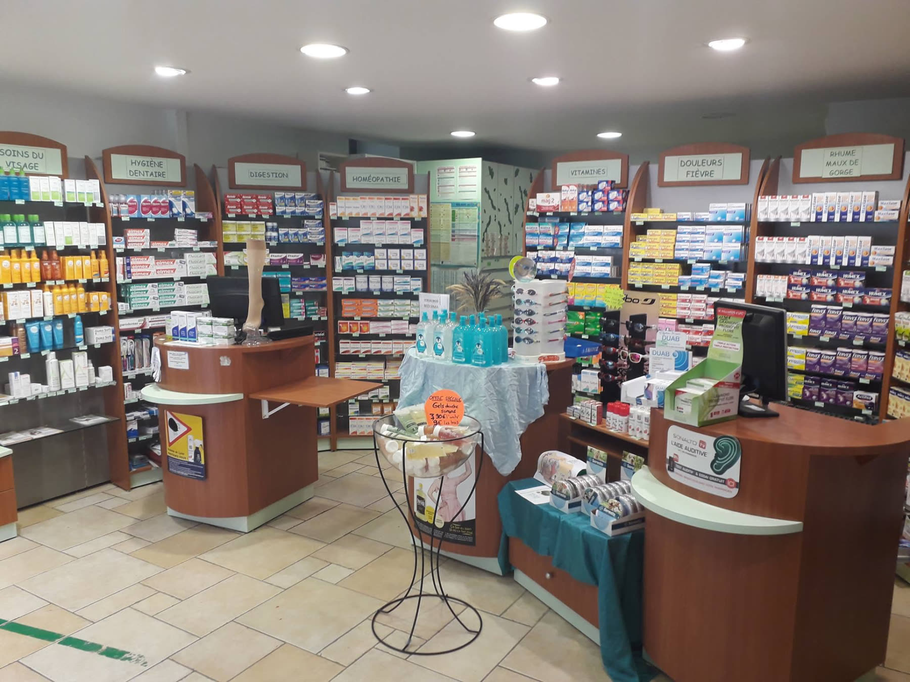 Vue d'ensemble de l'intérieur de la pharmacie avec ses rayons thématiques et son comptoir